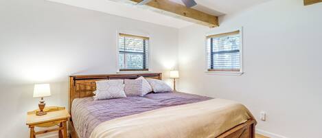 A bedroom with a wooden bed, two bedside tables with lamps, a ceiling fan, and two windows with blinds.