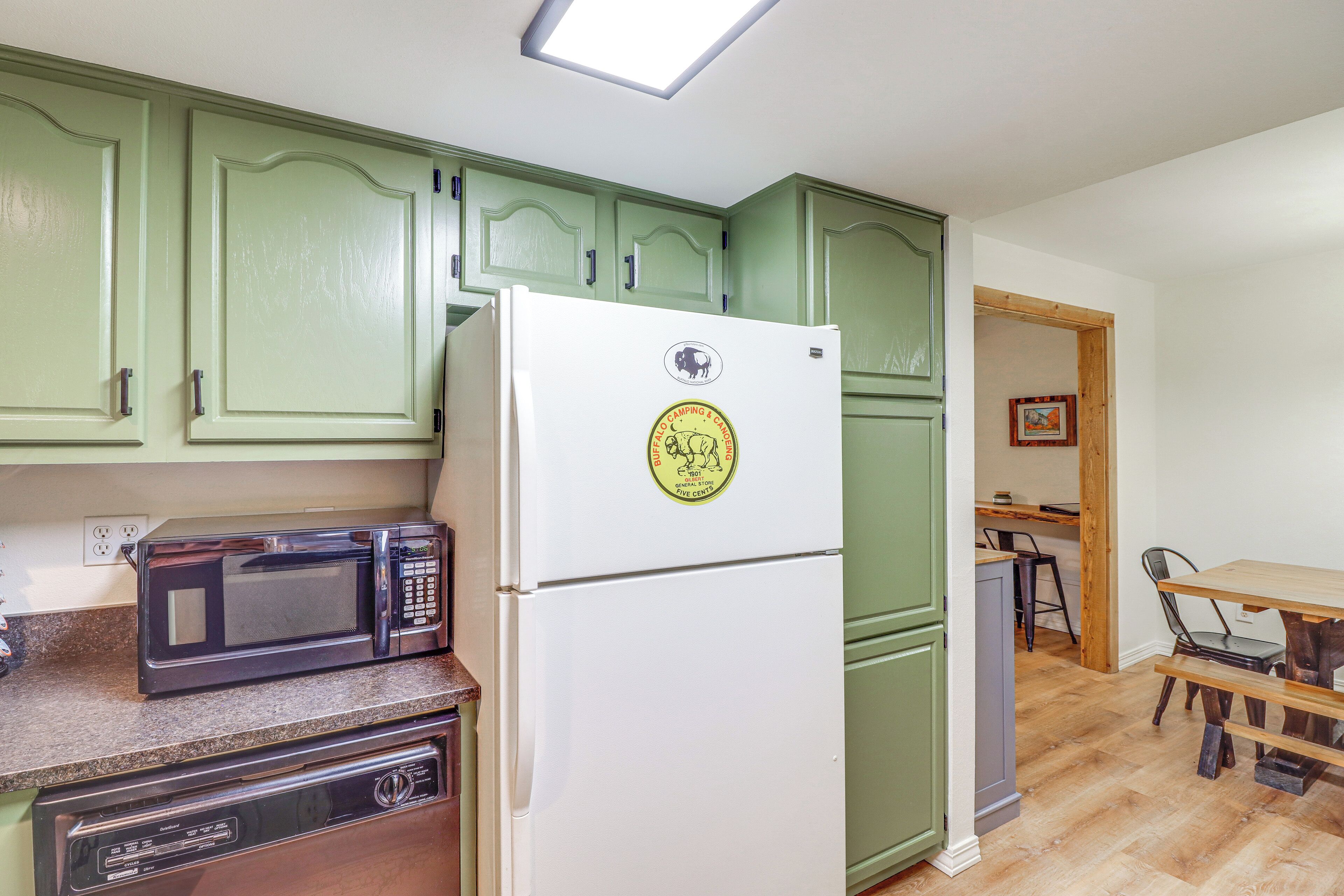 A kitchen with green cabinets, a white refrigerator, a black microwave, and a wooden dining table with chairs.