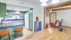 A modern kitchen with green cabinets, a wooden dining table, and a bar area with stools.