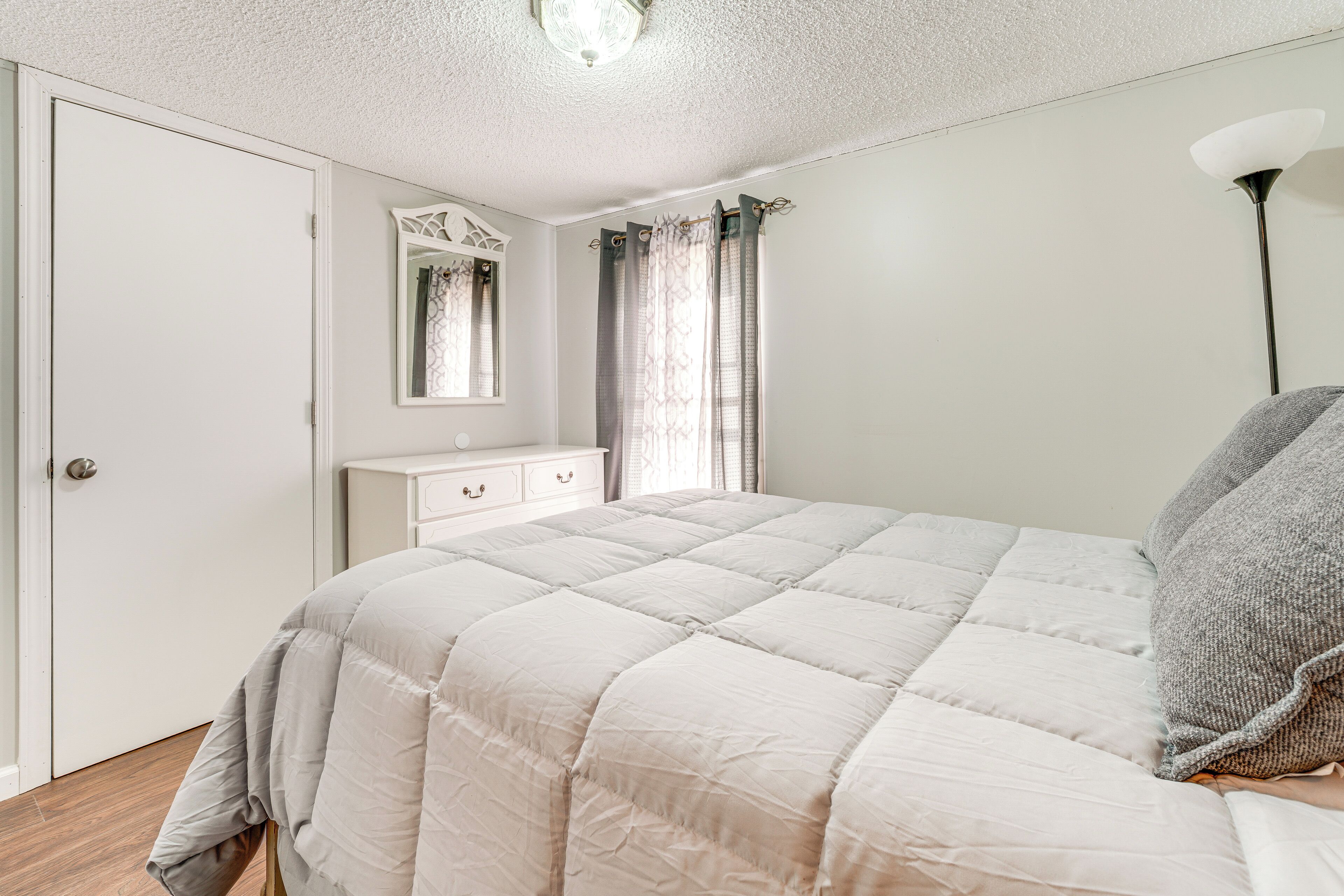 A bedroom with a bed, a dresser, a mirror, and a window with curtains.