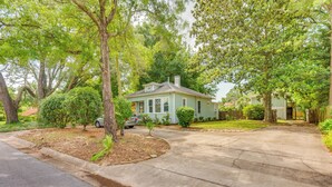 A residential street with a house featuring a front yard, driveway, and a parked car.