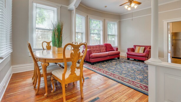 A spacious living room with a dining area, featuring a red sofa, wooden dining table, and a ceiling fan.