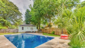 A backyard with a swimming pool, a wooden fence, and a small house.