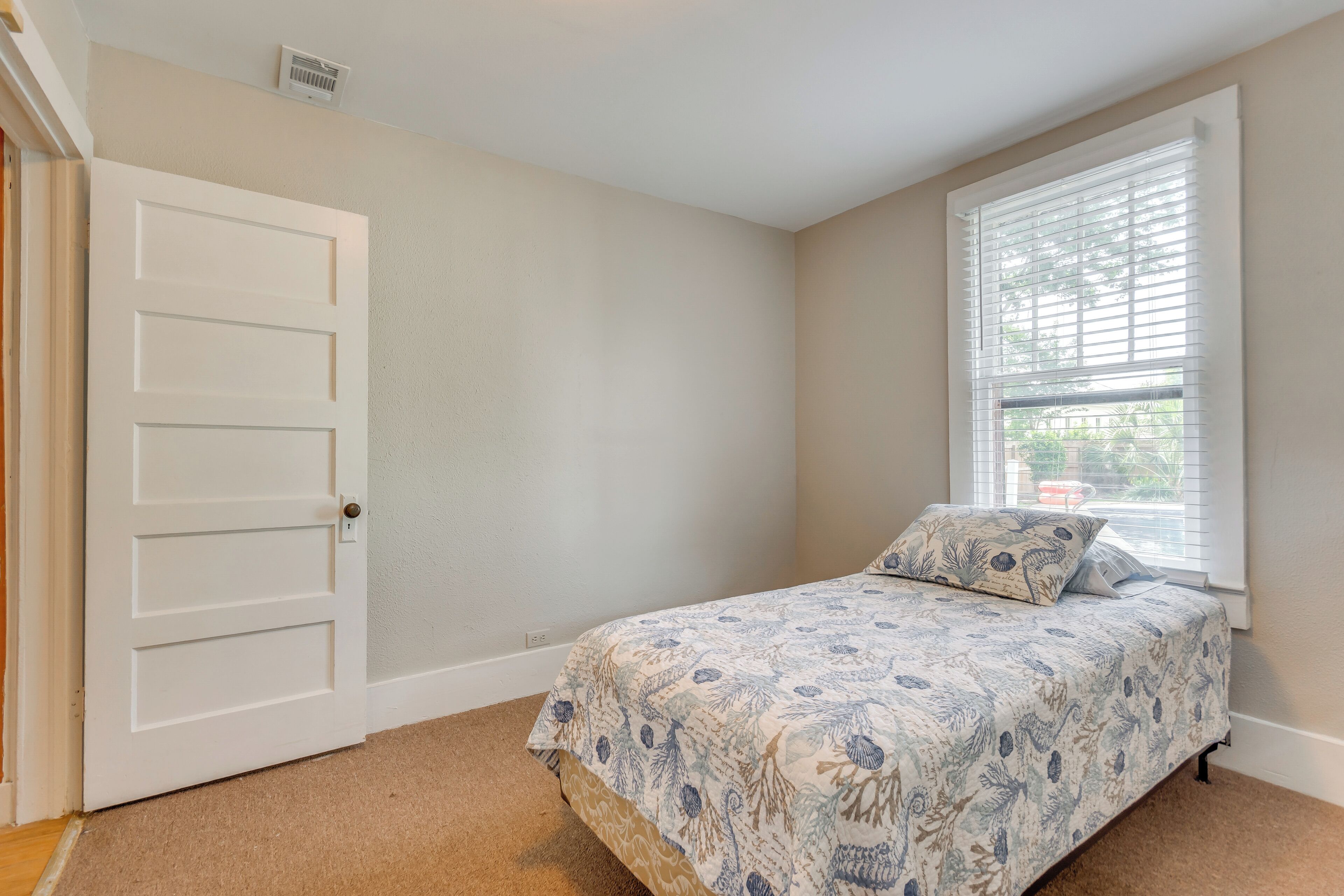 A bedroom with a bed, a window with blinds, a door, and a carpeted floor.