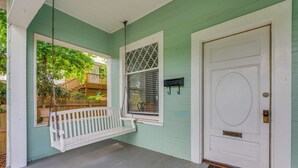 A porch with a white swing, a white door, and a window with a metal grille.