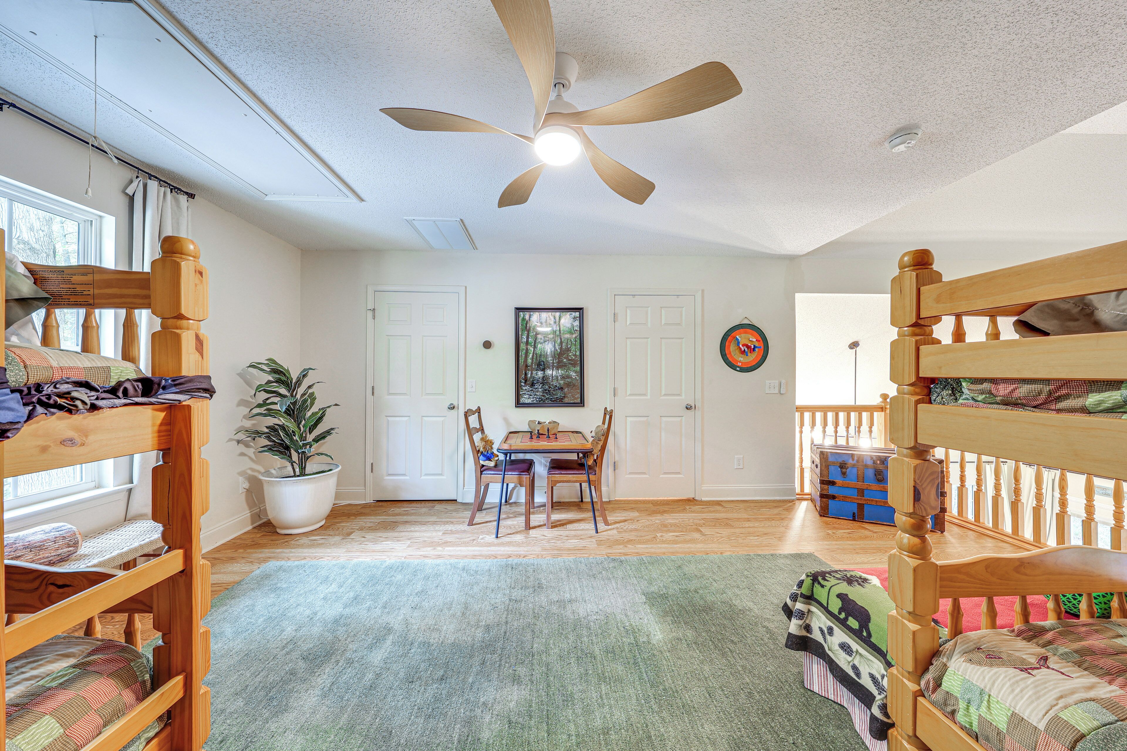 A room with bunk beds, a dining table, chairs, a ceiling fan, and a potted plant.