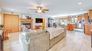 A spacious living room with a large beige sectional sofa, a fireplace, and a television. The kitchen is visible with wooden cabinets and stainless steel appliances. - Peaceful Family Home Near Cayuga Lake State Park (Seneca Falls)