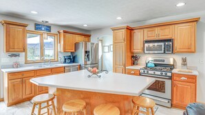 A spacious kitchen with wooden cabinets, a large island with stools, stainless steel appliances, and a view of the outdoors. - Peaceful Family Home Near Cayuga Lake State Park (Seneca Falls)