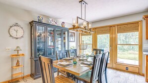 A dining area with a wooden table set for four, surrounded by chairs, a decorative cabinet with glass doors, and a large window with a view of greenery. - Peaceful Family Home Near Cayuga Lake State Park (Seneca Falls)