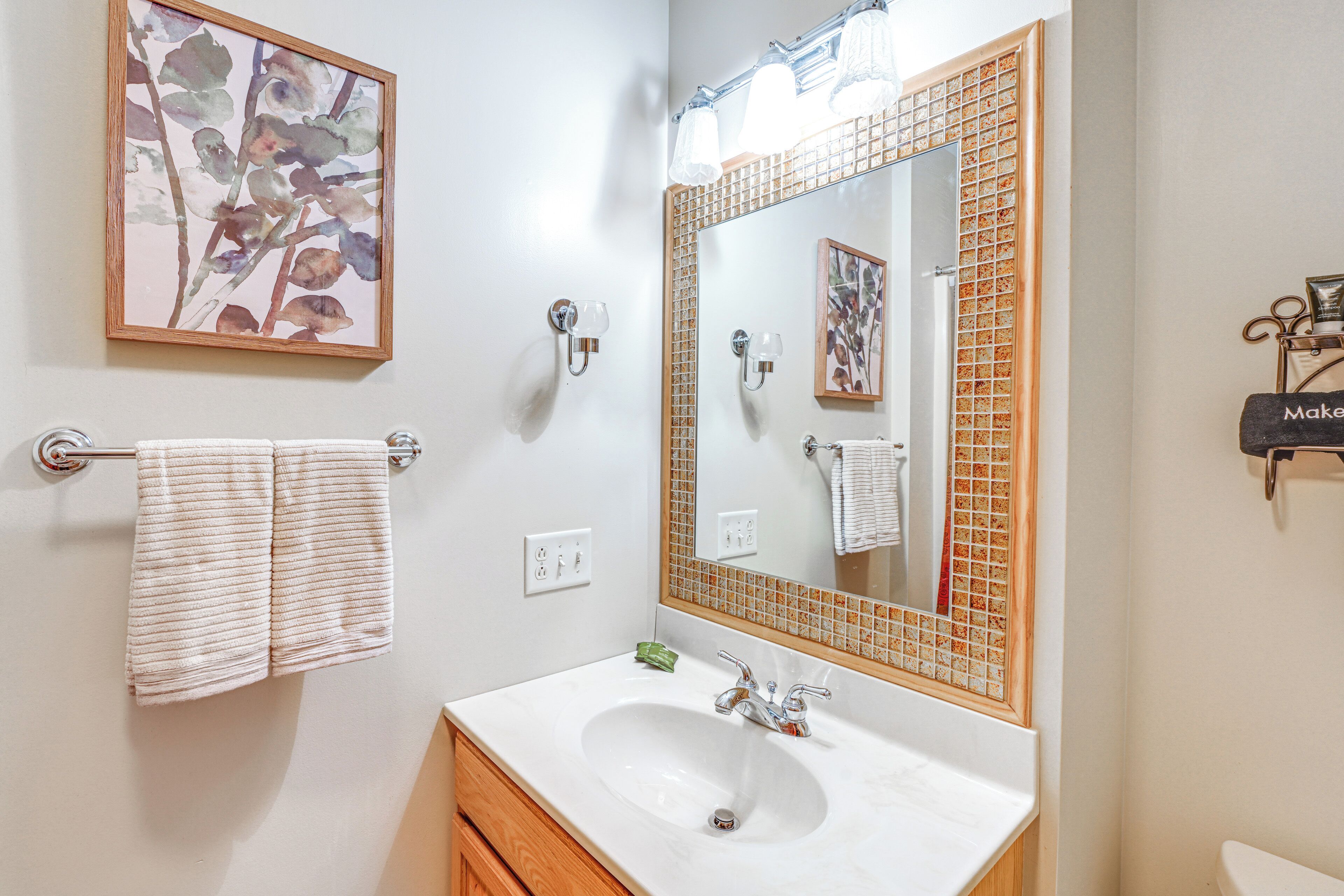 A bathroom with a white sink, a large mirror with a mosaic frame, and a towel rack with two towels.