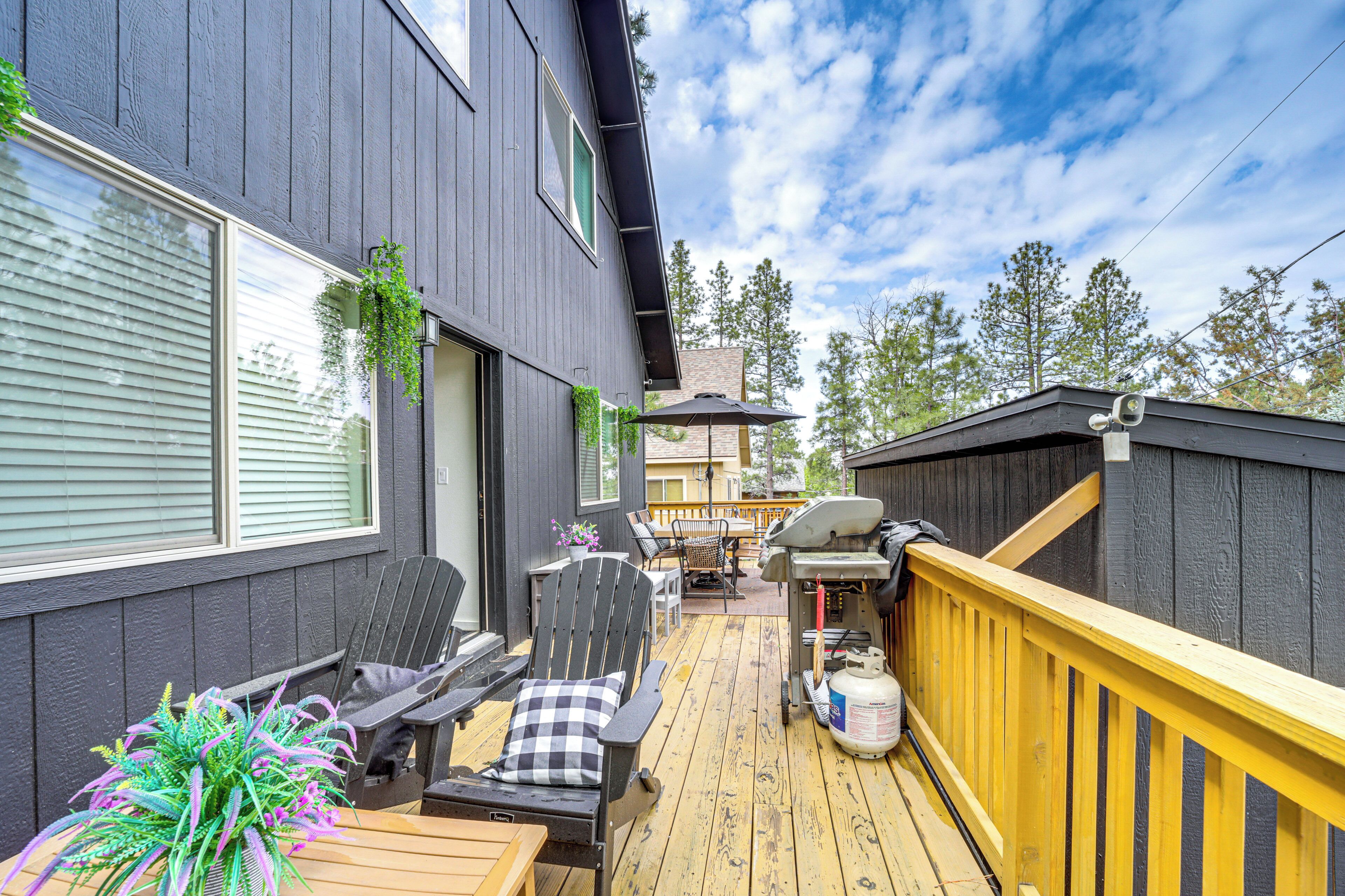 A wooden deck with outdoor furniture, a barbecue grill, and a view of the surrounding trees.