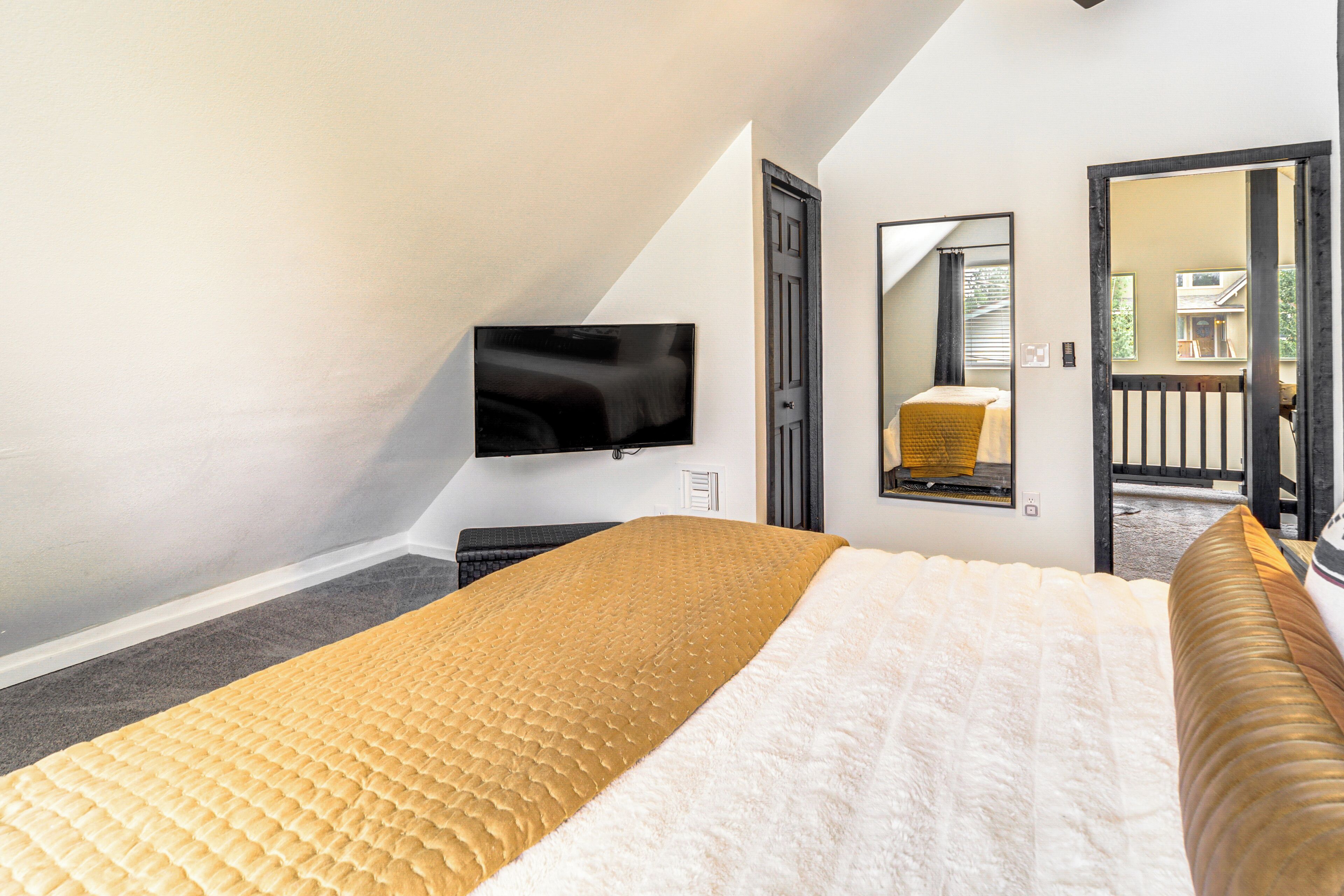 A bedroom with a bed, a television, a mirror, and a door leading to a balcony.