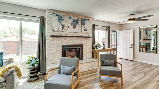 A living room with a fireplace, two grey armchairs, a coffee table, and a world map on the wall. - Newly Renovated Albuquerque Retreat w/ Pool Table (Albuquerque)