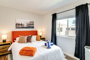 A hotel room with a large bed, a headboard, a nightstand with a lamp, a window with curtains, and a painting on the wall. - Newly Renovated Albuquerque Retreat w/ Pool Table (Albuquerque)