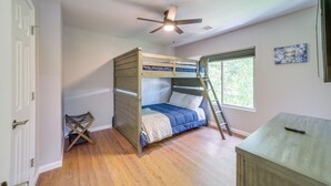 A bedroom with a bunk bed, a ceiling fan, a window, and a desk.