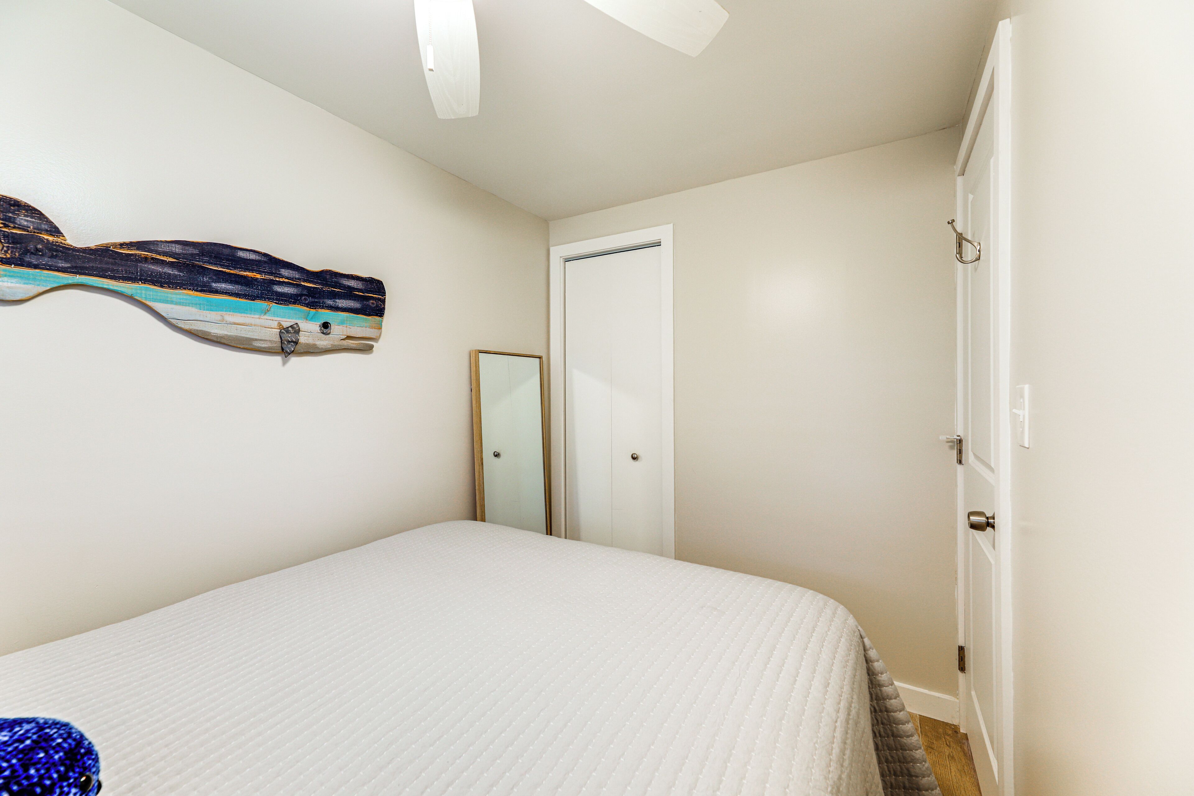 A bedroom with a bed, a door, a mirror, and a wall-mounted artwork.