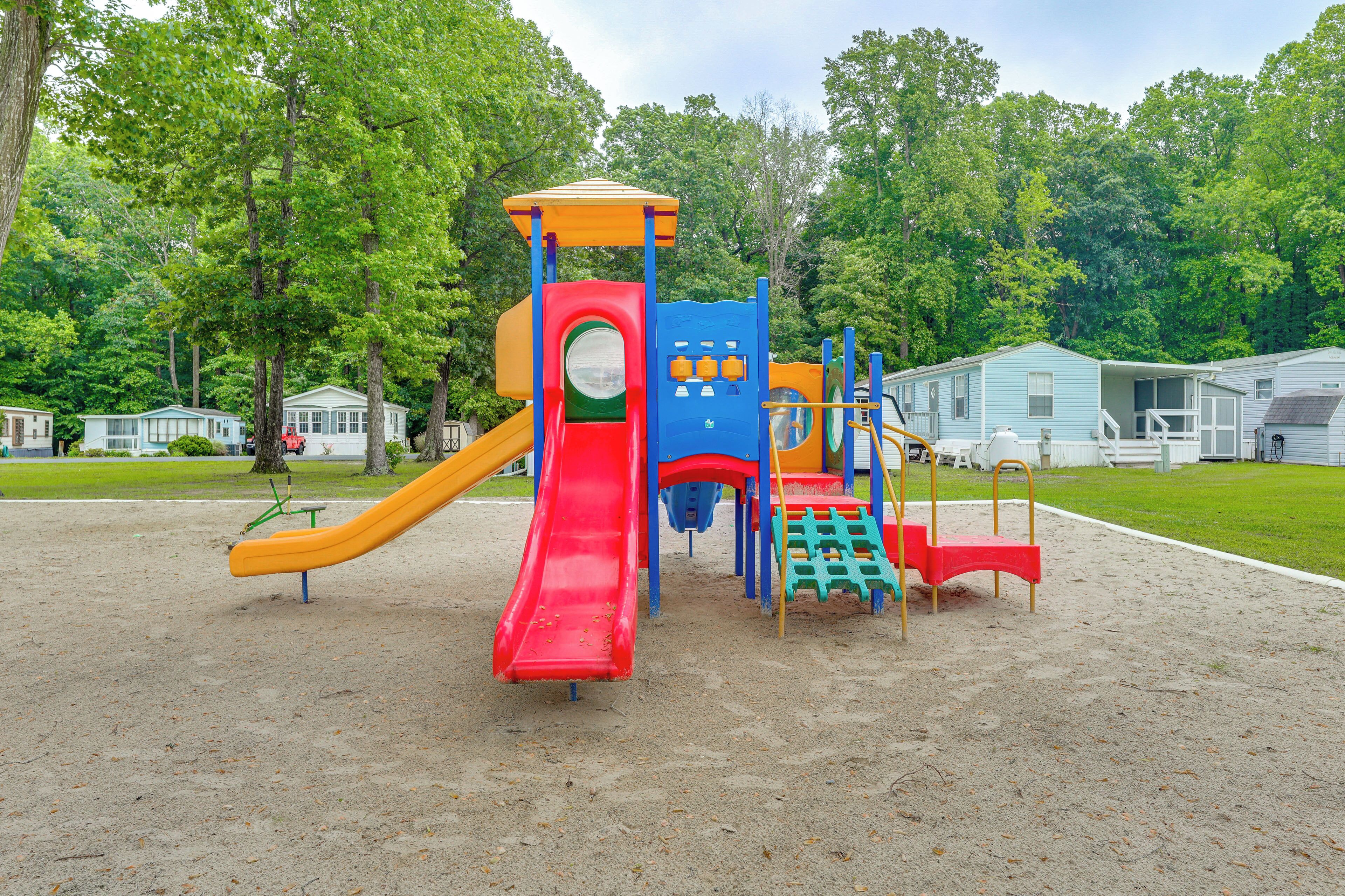 A playground with slides and climbing structures, surrounded by trees and houses.