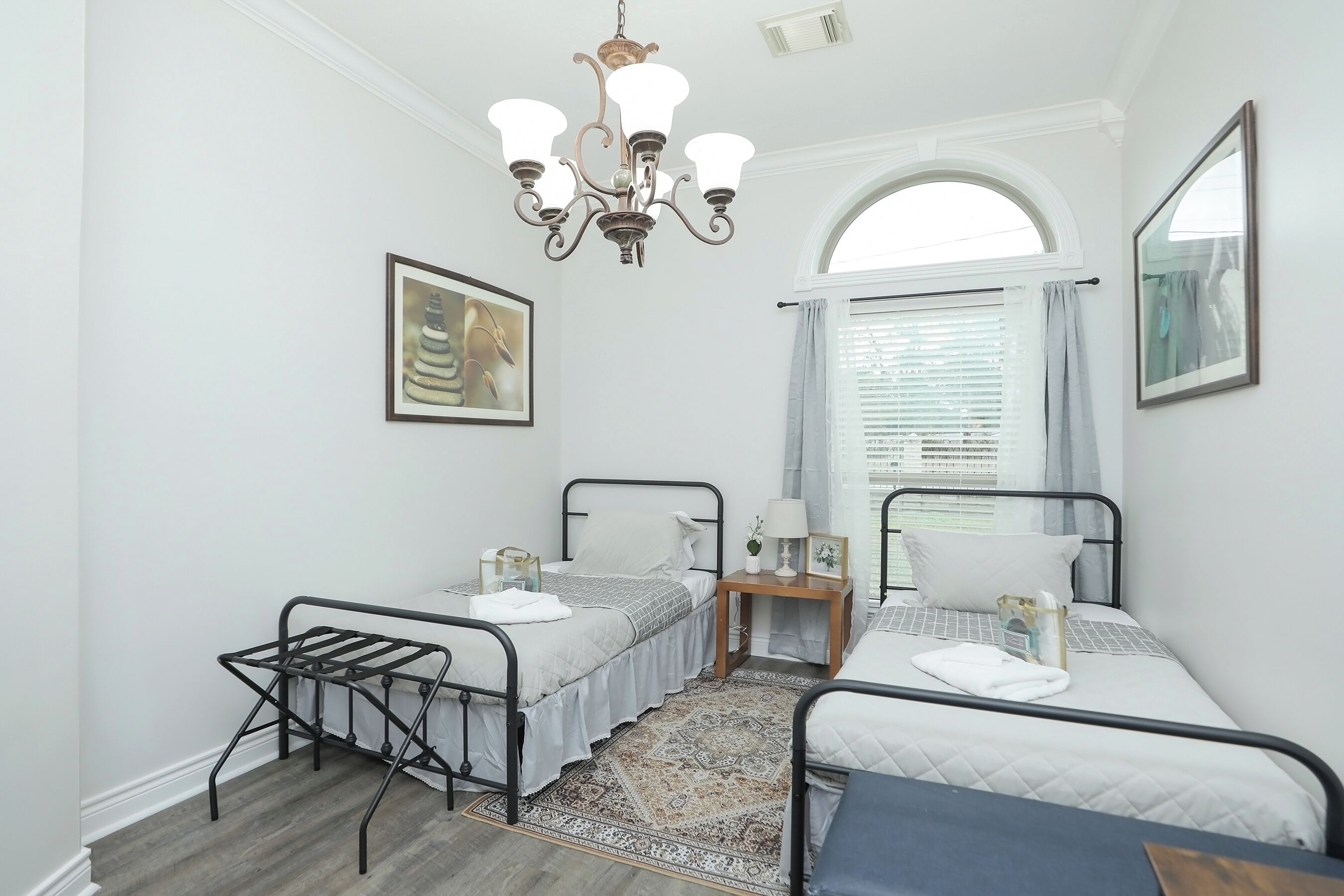 Une chambre avec deux lits, un lustre, une fenêtre avec des rideaux et un tapis.