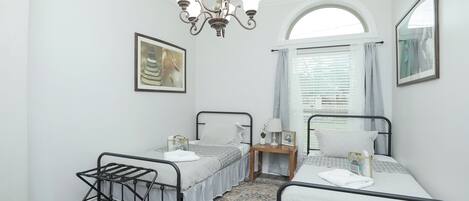 Une chambre avec deux lits, un lustre, une fenêtre avec des rideaux et un tapis.