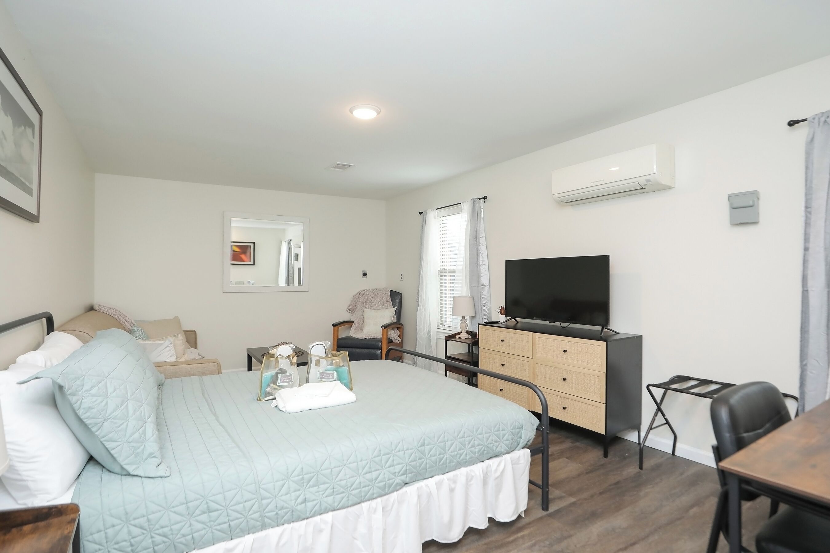 A neatly arranged bedroom with a bed, bedside table, dresser, and a TV.