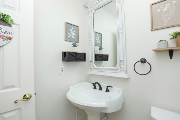 Une salle de bain avec un lavabo blanc, un miroir, un porte-serviettes et une petite étagère sur laquelle est posée une plante.