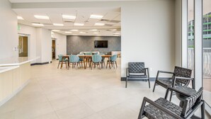 Un hall d’entrée spacieux avec un comptoir de réception, un espace repas avec des tables et des chaises, et une grande fenêtre donnant sur la façade de l’immeuble.