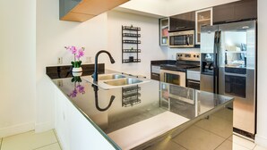 Une cuisine moderne dotée d’appareils électroménagers en acier inoxydable, d’un îlot central en verre et d’une étagère en métal noir.