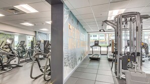 Une salle de sport équipée de tapis de course, de vélos elliptiques et d’une machine de musculation.