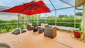 Un patio techado al aire libre con muebles de mimbre, un paraguas rojo y vistas a la vegetación y casas.