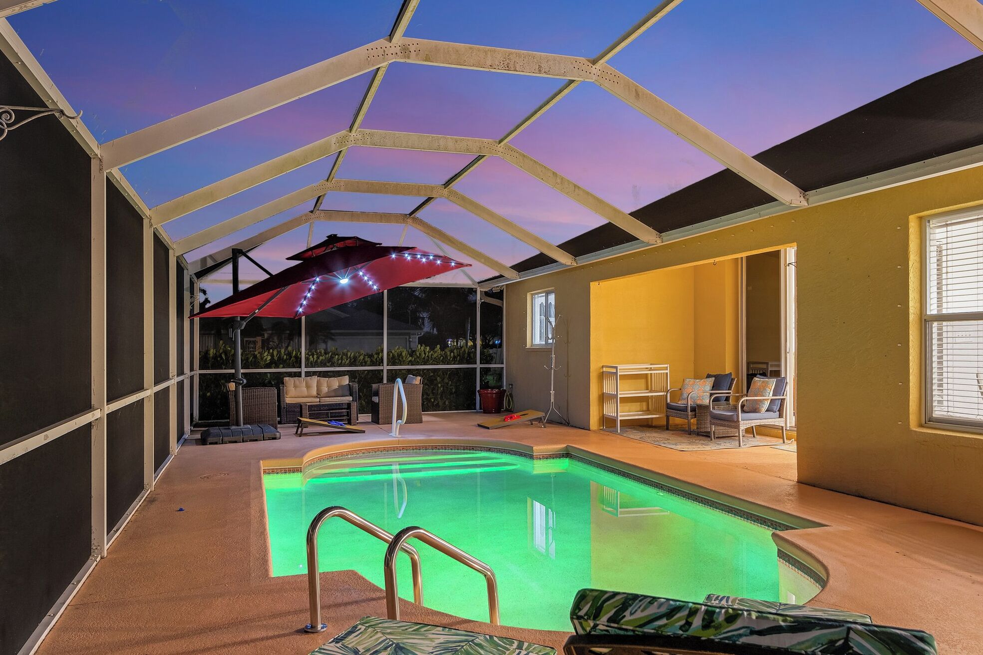 A covered swimming pool area with a glass ceiling, a red umbrella, and seating arrangements.