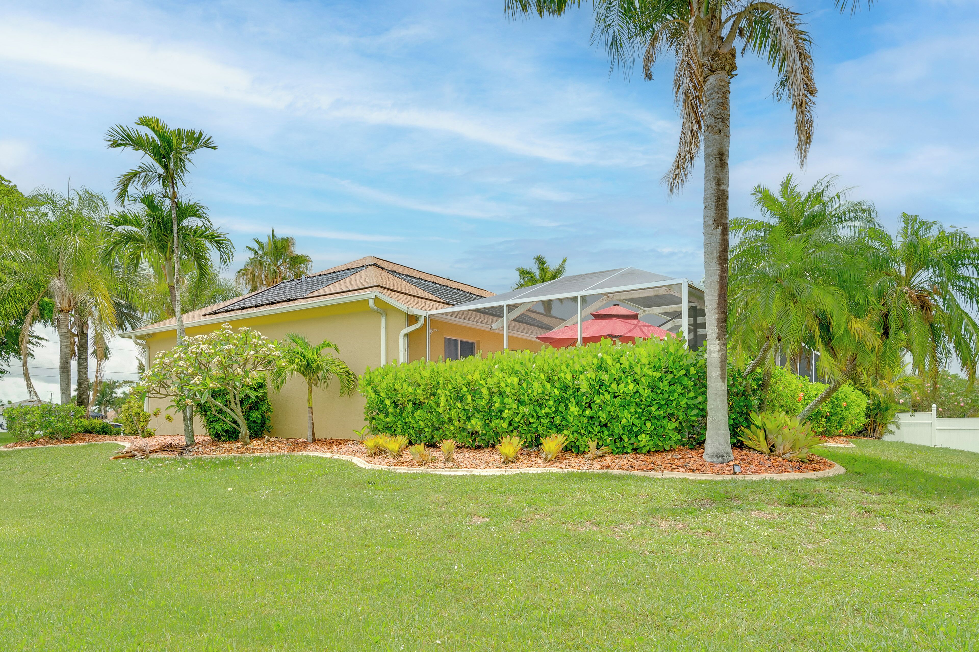 A house with a covered patio, surrounded by well-maintained lawns and palm trees.