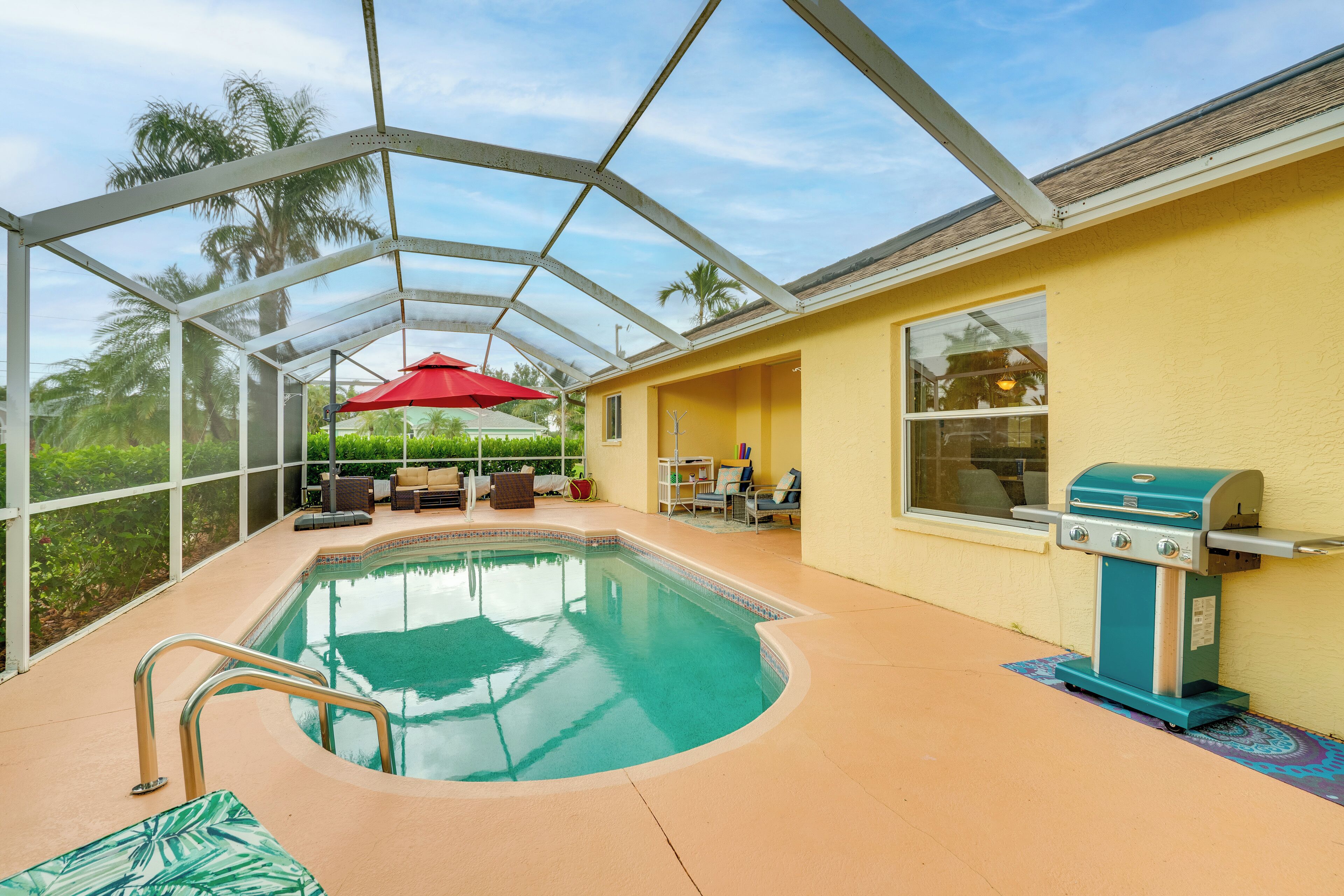 An indoor pool area with a glass enclosure, a red umbrella, and a barbecue grill.