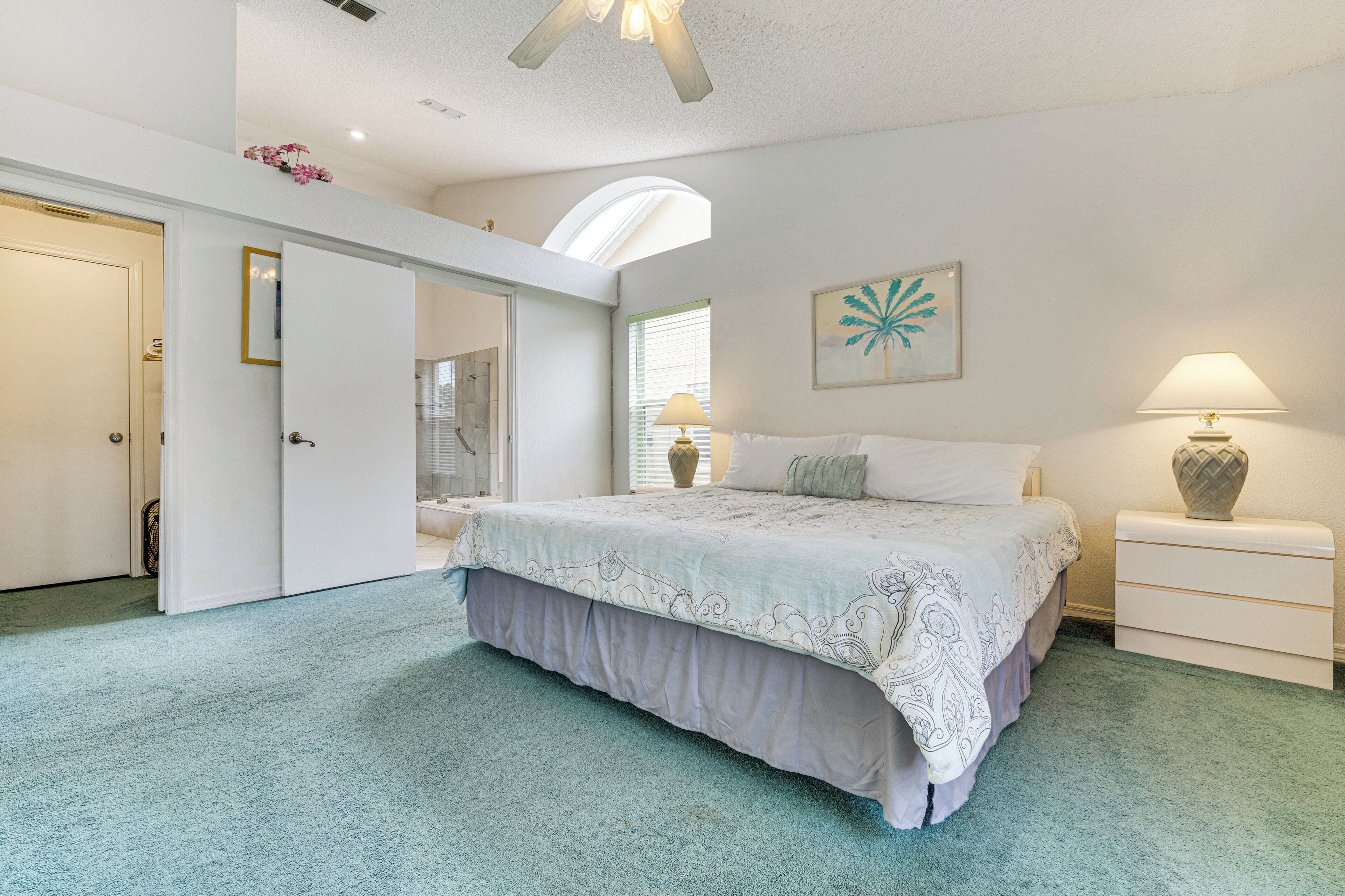 A bedroom with a bed, a nightstand, a lamp, a painting, and a door leading to another room.