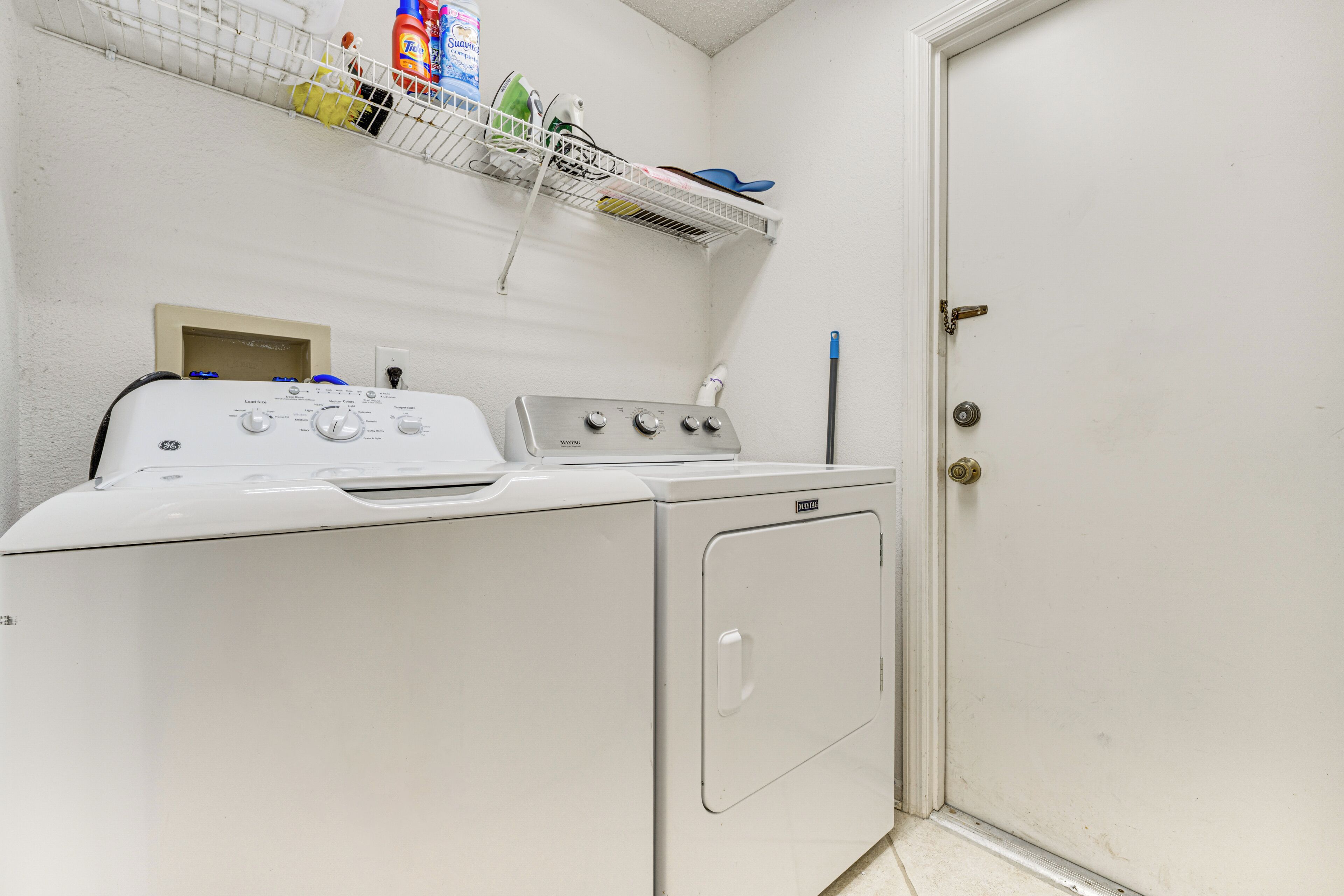 A laundry area with a washing machine, dryer, and a shelf above containing cleaning supplies.