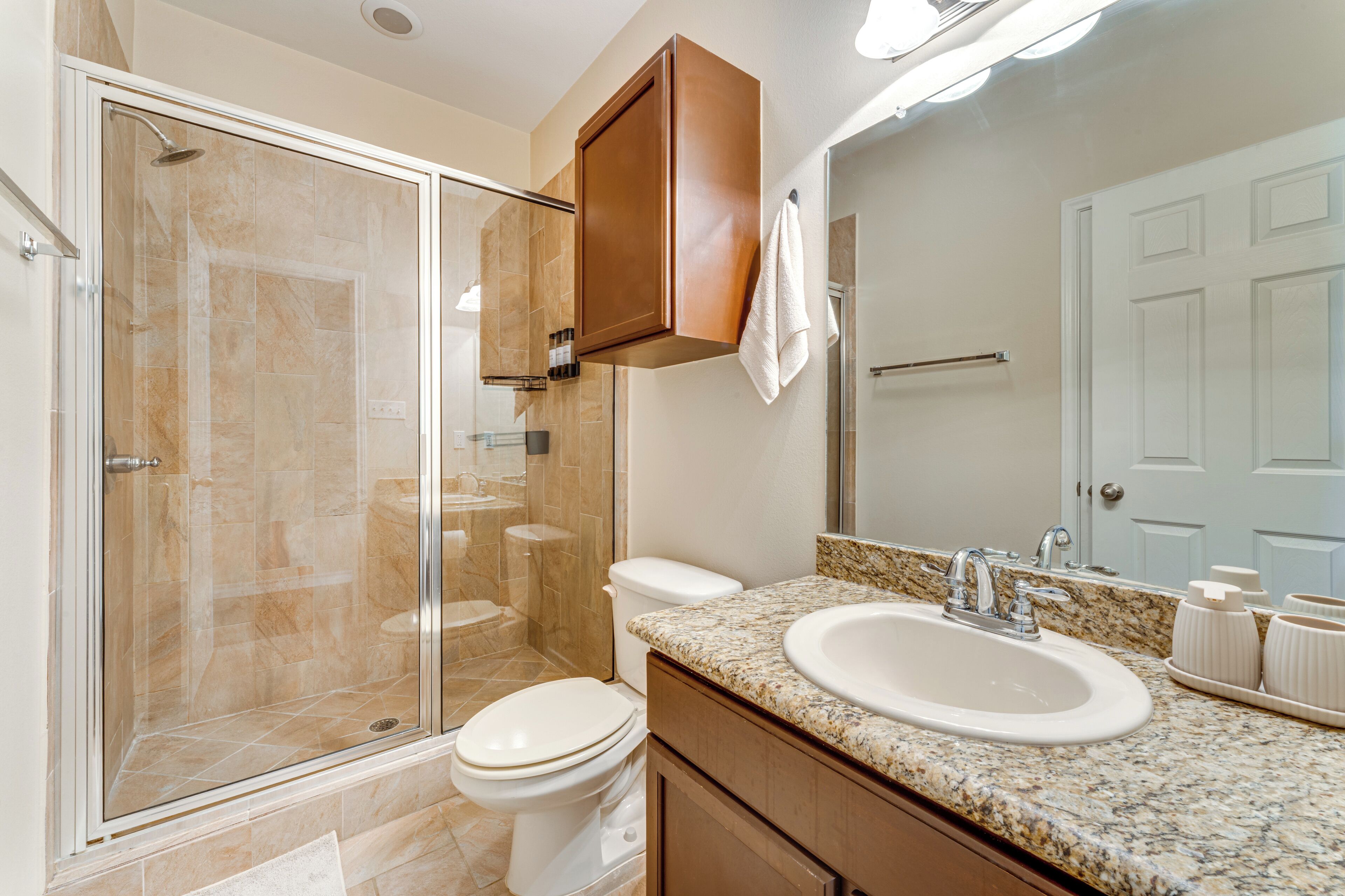 Une salle de bain moderne dotée d’une douche à parois de verre, de toilettes blanches, d’un lavabo avec un plan de travail en marbre et d’un grand miroir au-dessus du lavabo.