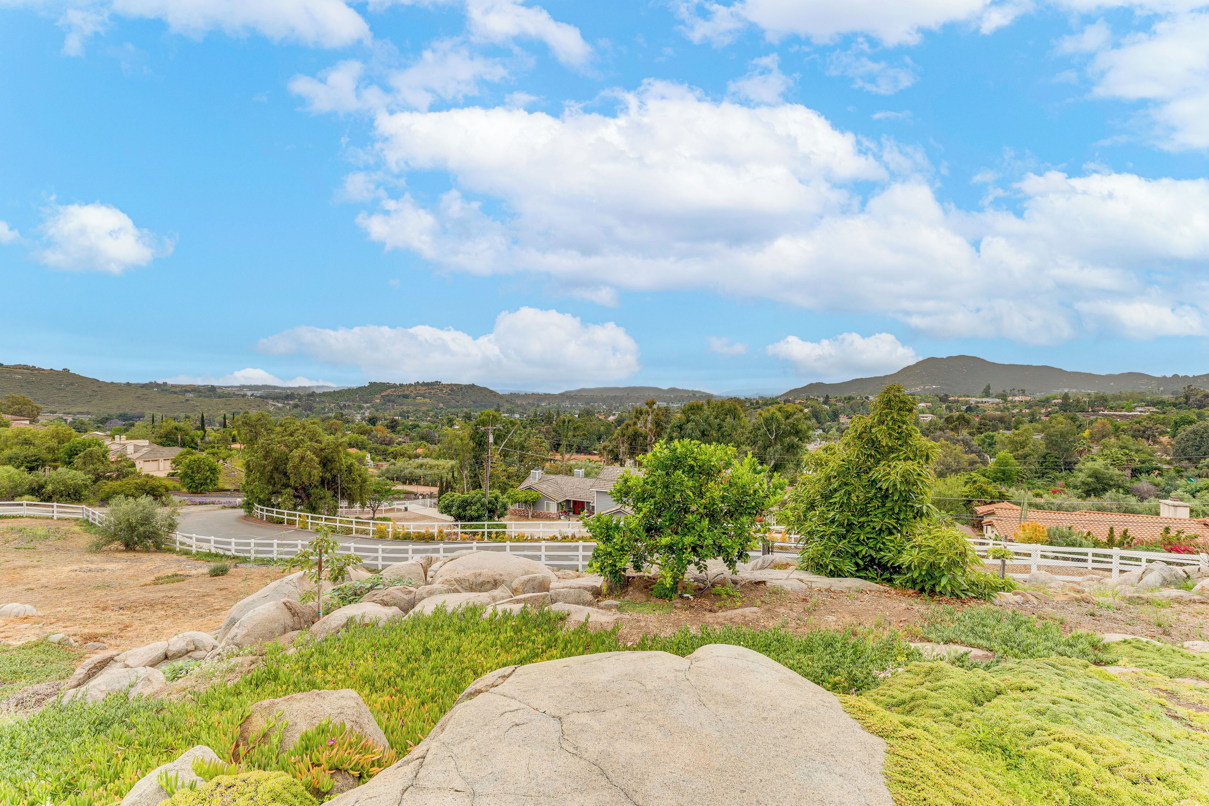 Paisaje con colinas ondulantes, una cerca blanca y una casa con techo rojo.