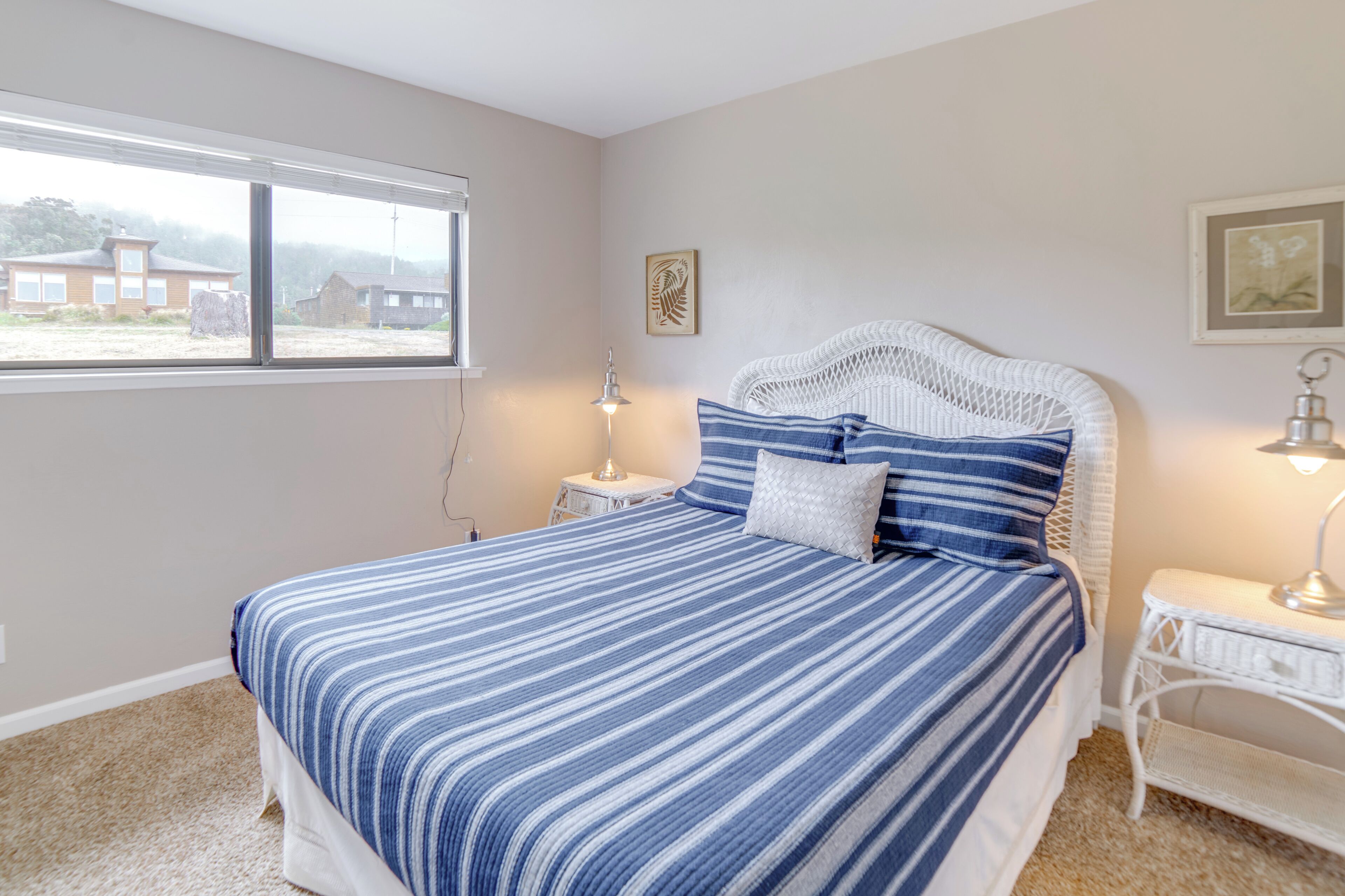 A bedroom with a bed, a nightstand, a lamp, and a window with a view of buildings.