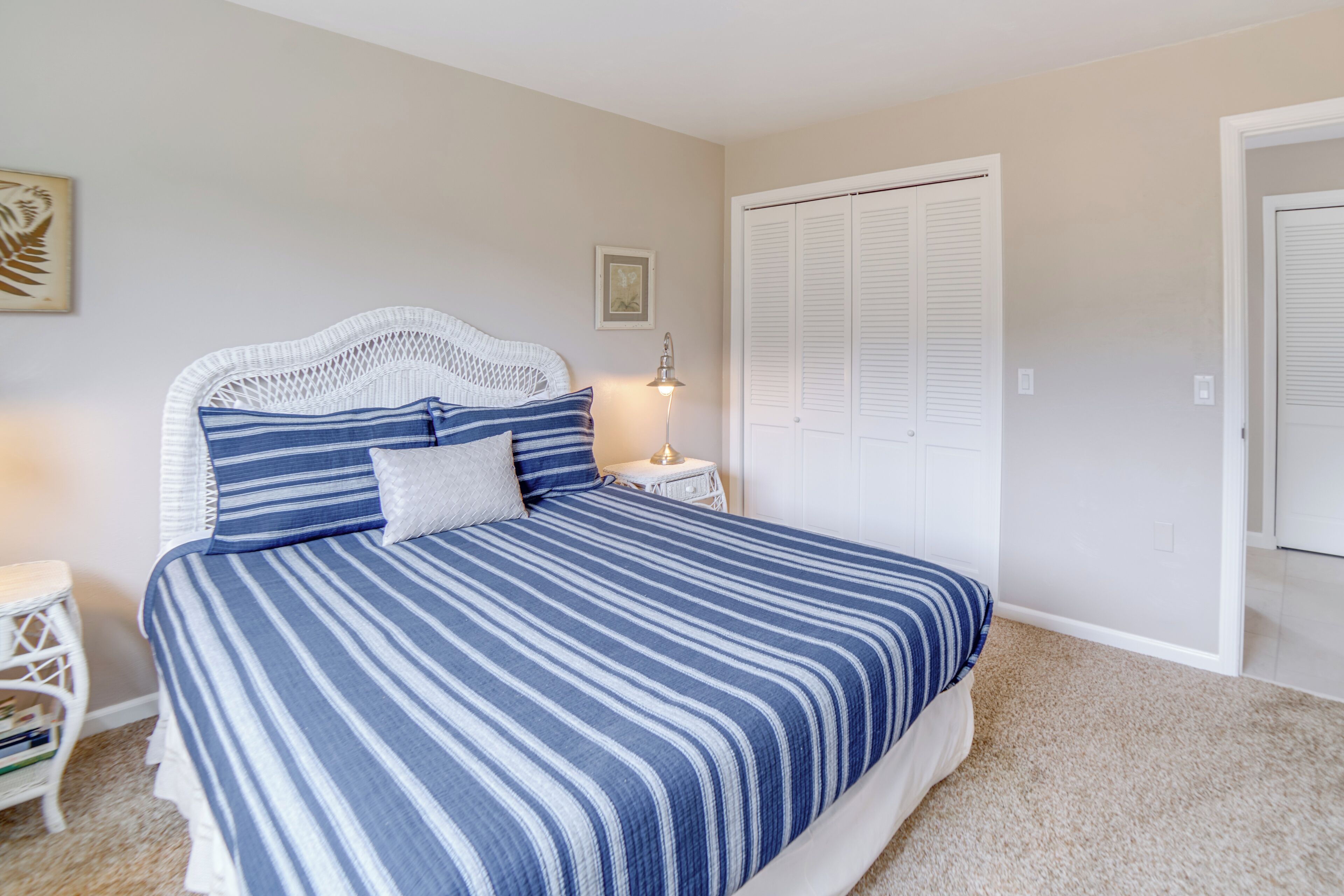 A neatly made bed with a striped blue and white comforter, a white headboard, and a bedside table with a lamp.