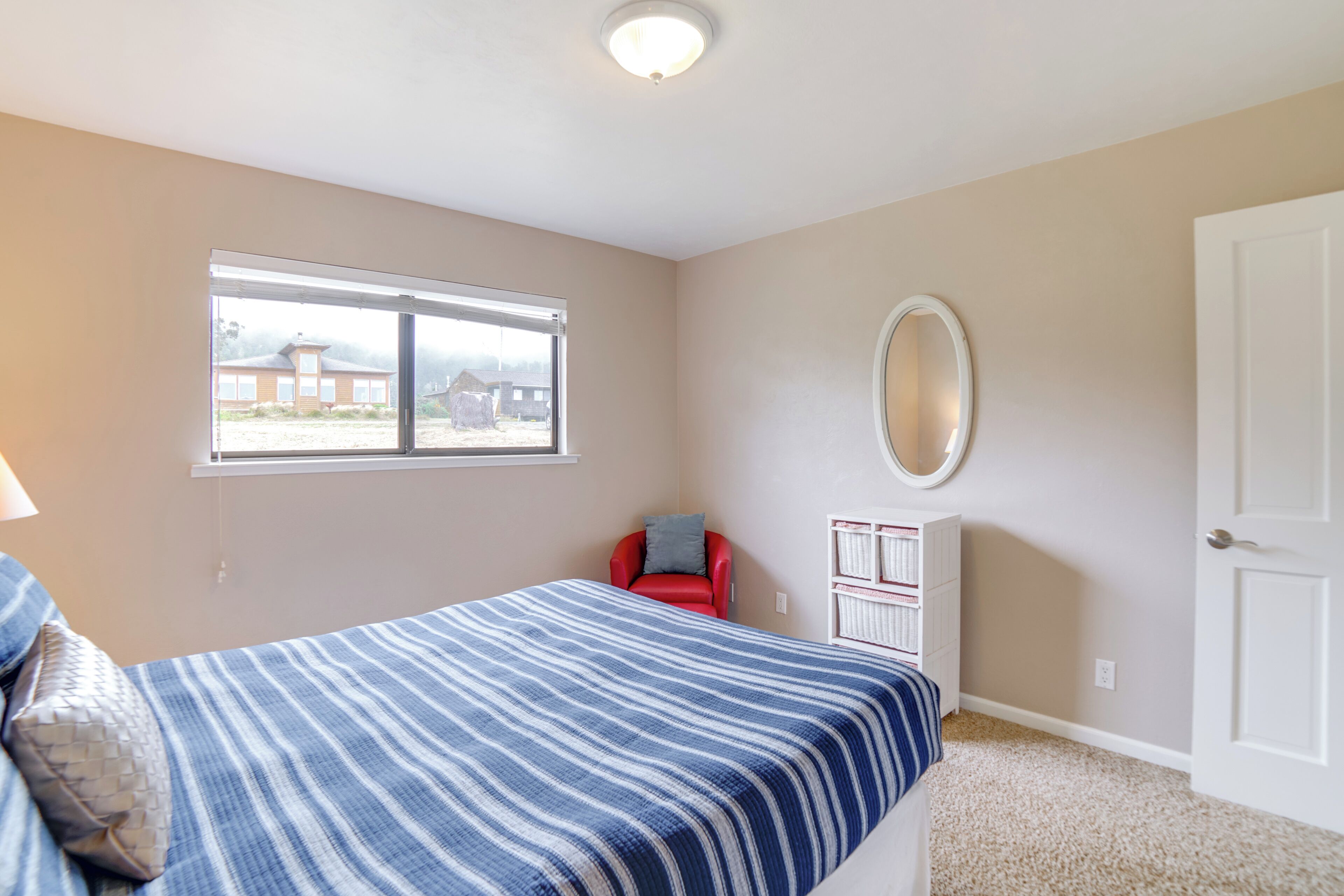A bedroom with a bed, a window, a red chair, a white cabinet, and a door.