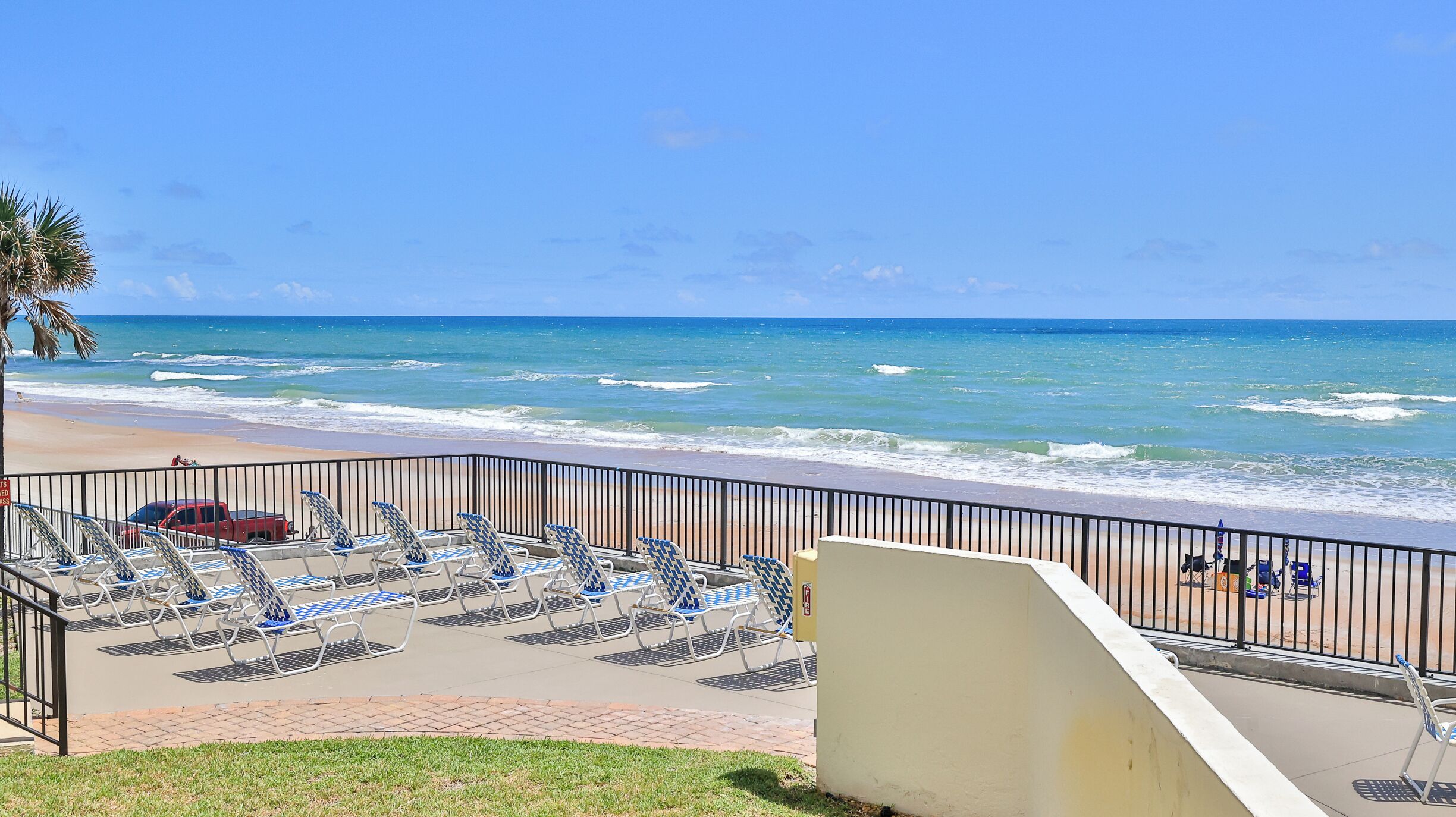 A beach view with lounge chairs and a parking area.
