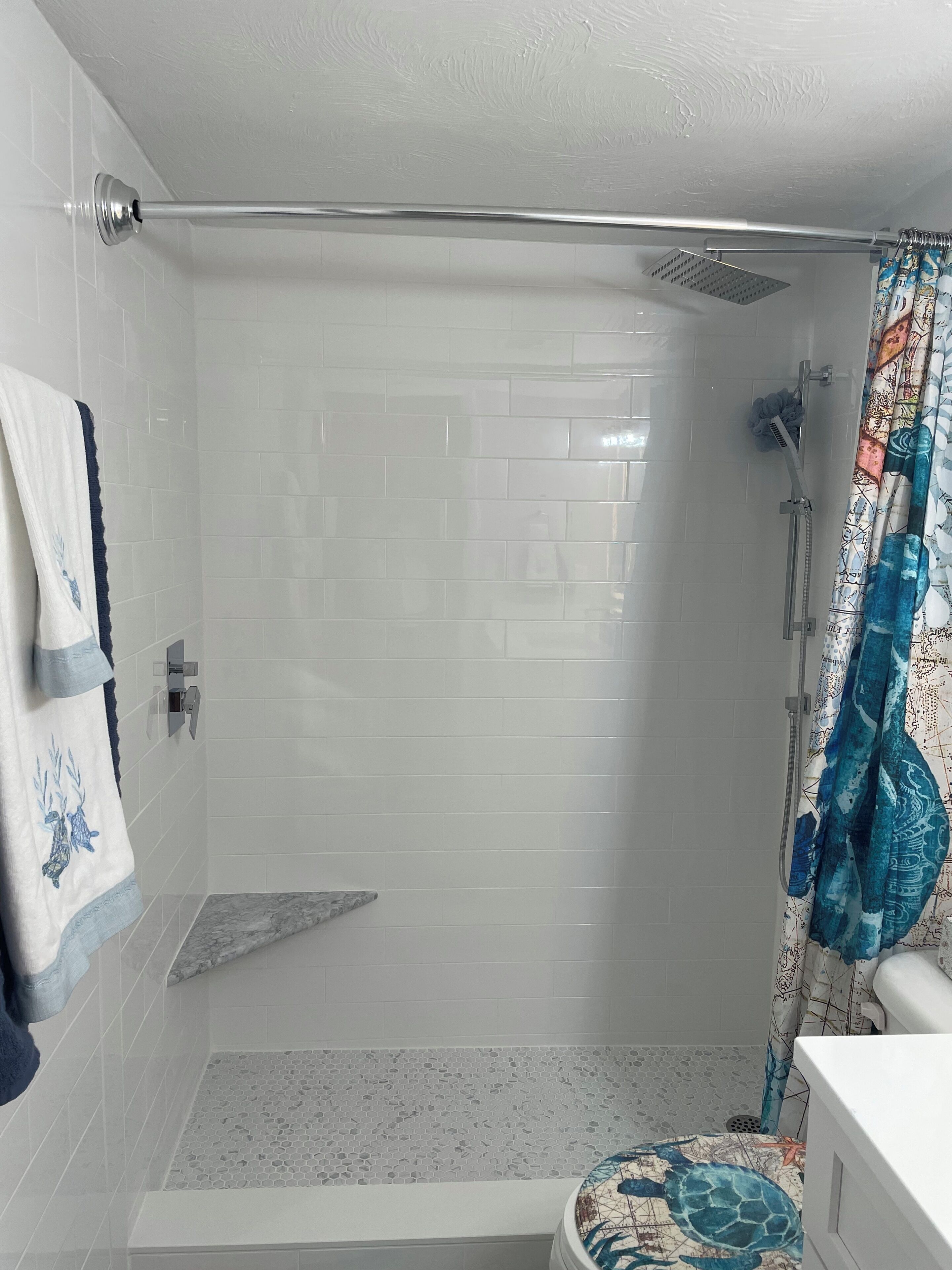 Un baño moderno con paredes de azulejos blancos, una ducha con puerta de cristal, suelo de mármol y cortina de baño colorida.