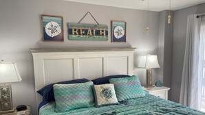 Une chambre à coucher comprenant un lit, deux tables de chevet, une commode, une lampe fixée au mur et une fenêtre avec des rideaux.