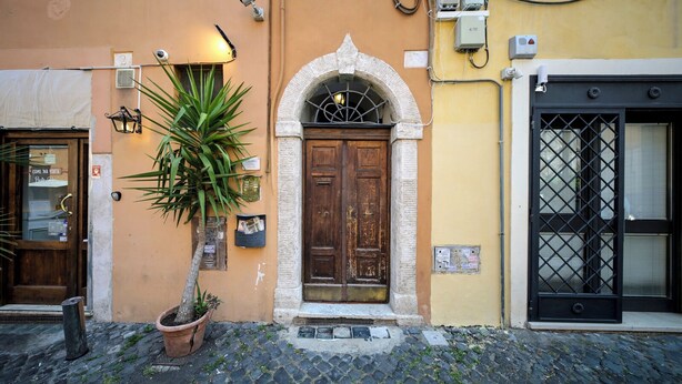 Une rue pavée avec un bâtiment doté d’une porte en bois, d’un pot de fleurs et d’une caméra de surveillance.