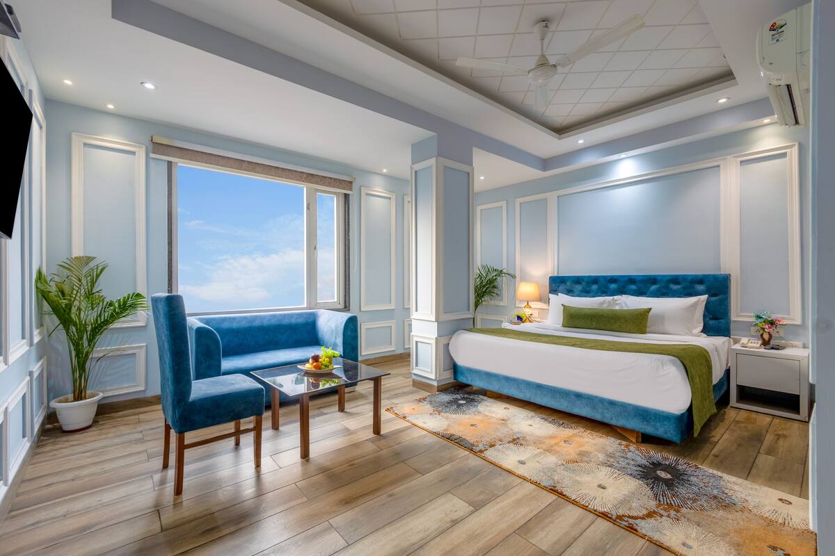 Una camera d'albergo moderna con un letto grande, un divano blu, un tavolino con della frutta e vista sul cielo.
