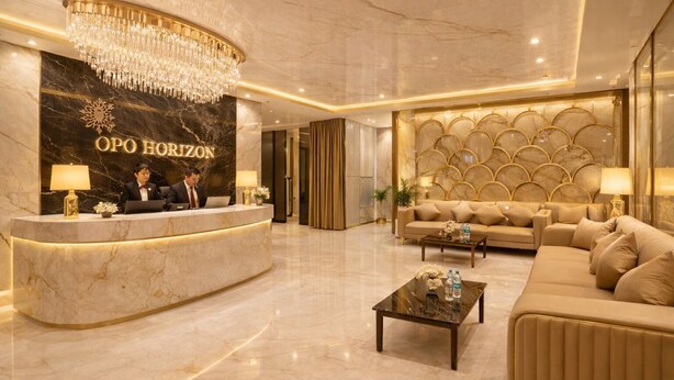 A hotel lobby with a reception desk, a chandelier, a sofa, and a coffee table.