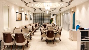A spacious hotel dining area with multiple round tables and chairs, a modern chandelier, and framed artwork on the walls.