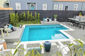 A rectangular pool with a tiled deck, surrounded by a black fence, a seating area with cushions, and a dining set. - Luxe 19BR Suit | Private Backyard with Pool (New Orleans)