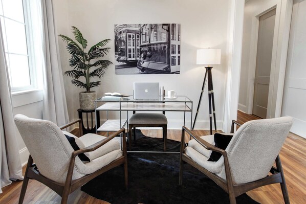 Ein moderner Arbeitsraum mit einem Glastisch, zwei Polsterstühlen, einem Laptop, einer Topfpflanze und einer Stehlampe.