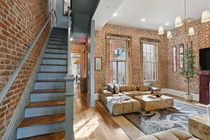 Un salon spacieux avec un mur en briques, un escalier en bois et une grande fenêtre.