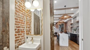 Un baño moderno con pared de ladrillo rústico, un lavamanos blanco y un espejo con marco dorado.